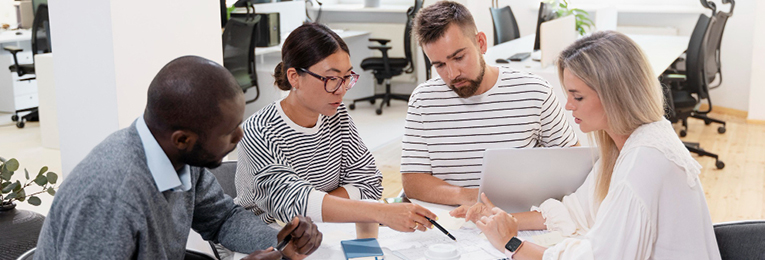 Four team members are seen engaging in a discussion around a table in an office space.